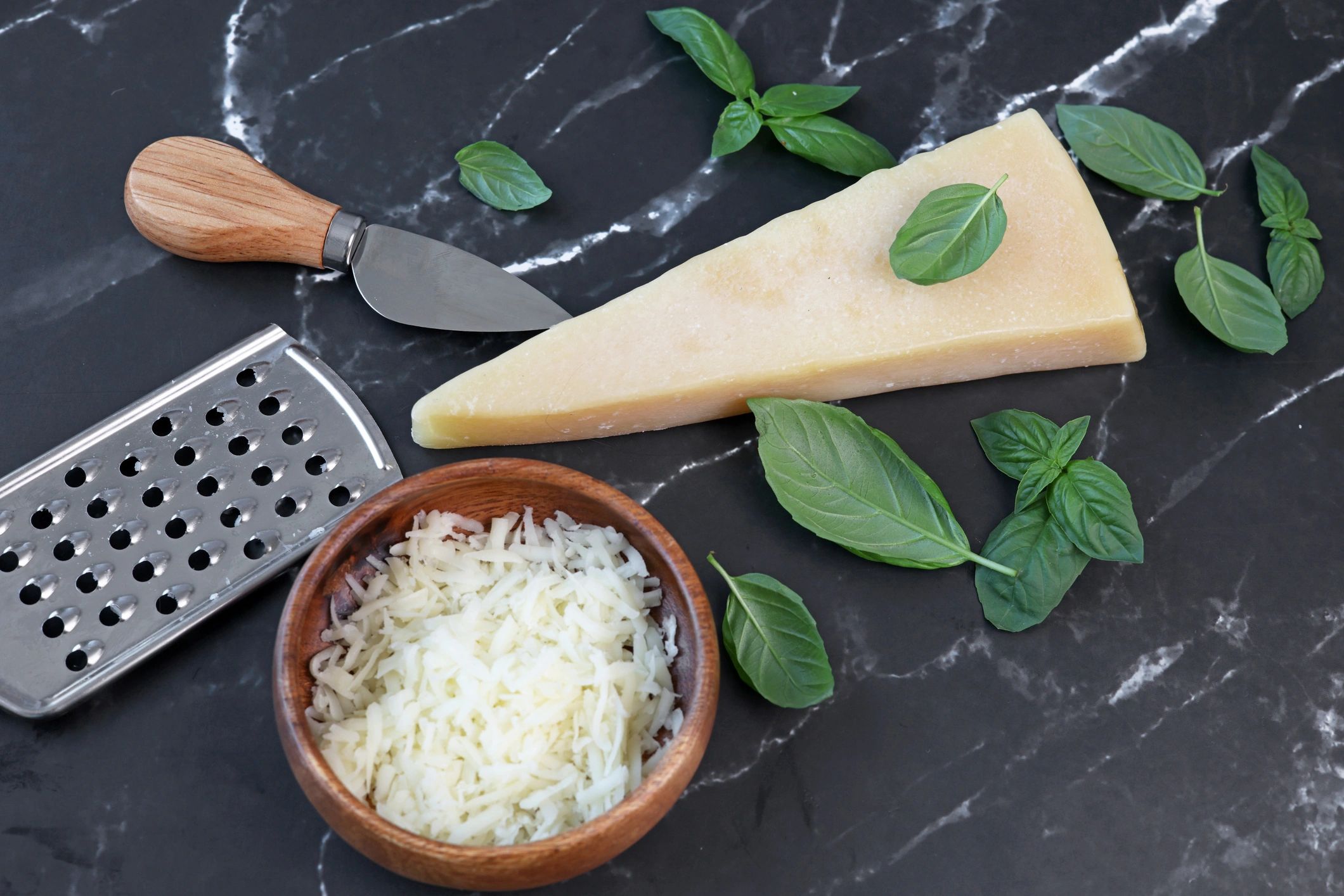 Fresh cooking ingredients including basil and parmesan on a dark surface
