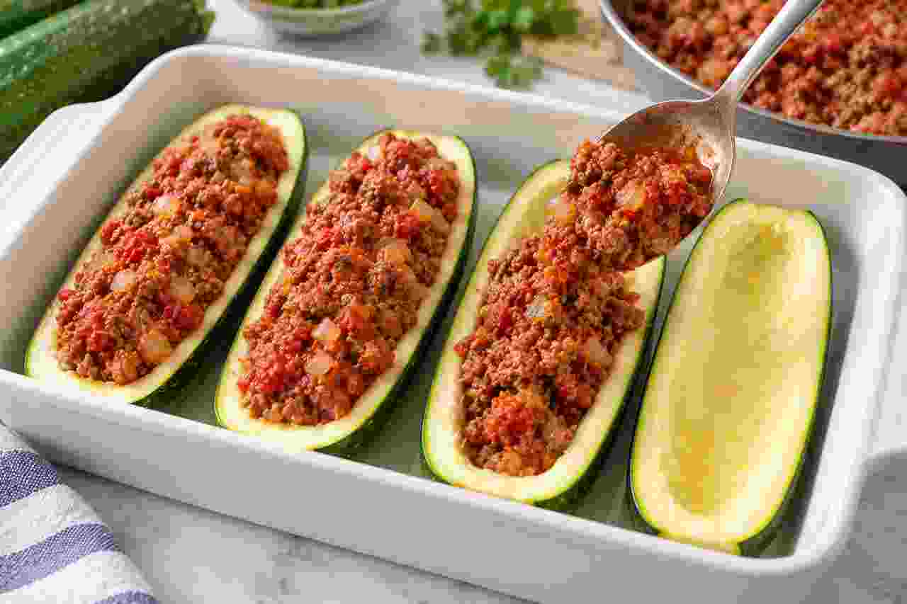 Seasoned ground beef and tomato filling being spooned into hollowed zucchini boats