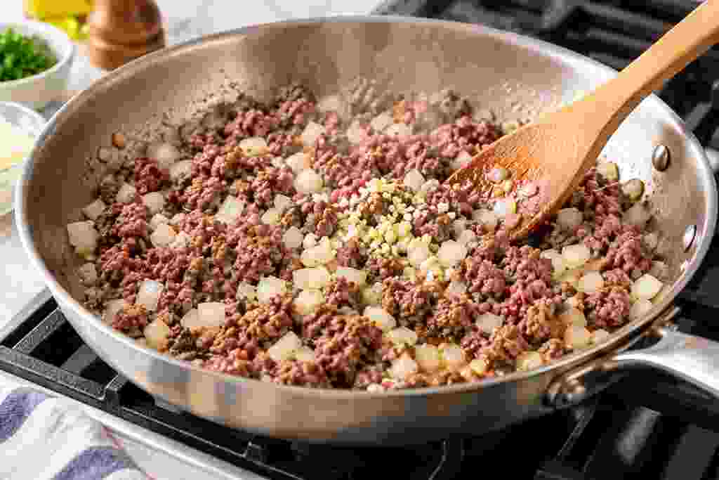 Lean ground beef cooking with diced onion and minced garlic for stuffed zucchini boats